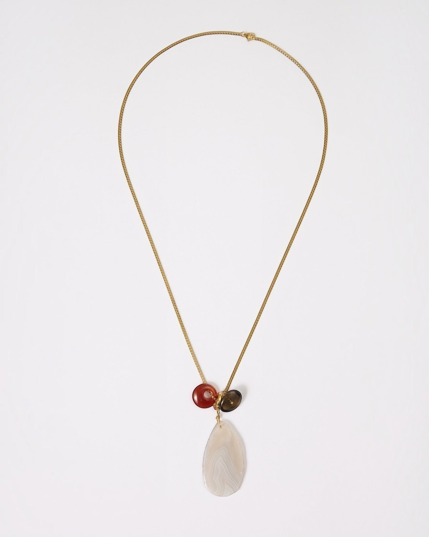 Elsita Jewelry Glacier Day necklace featuring a white agate slice, red agate ring, and smoky quartz on a gold chain.