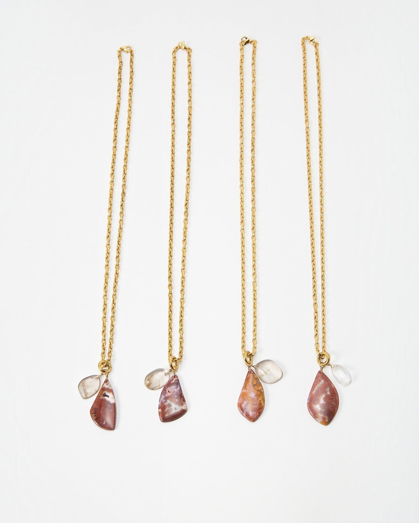 Four Elsita Jewelry Drift necklaces featuring gold chains and multi-colored stone pendants on a white background.