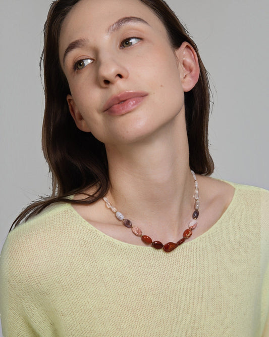 Elsita Jewelry Glow necklace featuring a gradient of red agate, jasper, and clear quartz beads on a model