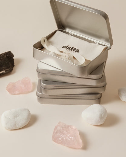 Elsita Jewelry branded metal tins containing Wild 1 agate earrings, displayed with raw rose quartz and white stones.