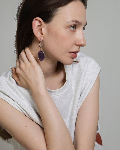 Elsita Jewelry Calm amethyst drop earrings featuring deep violet geometric stones on silver hoops worn by a model.