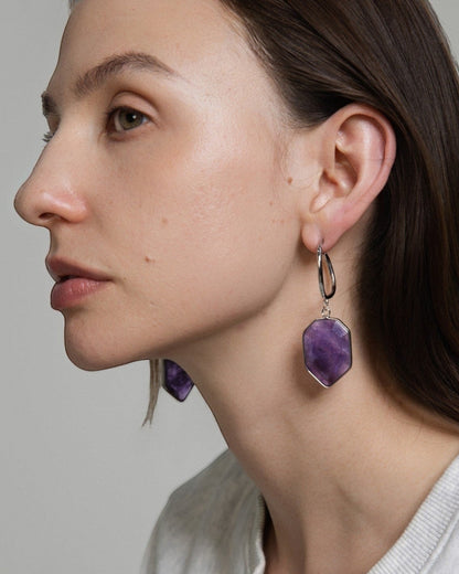 Elsita Jewelry Calm amethyst earrings featuring geometric violet stones on silver hoops worn by a woman in profile.