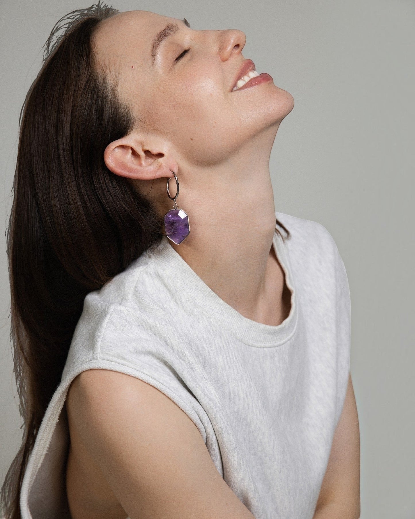 Elsita Jewelry Calm amethyst geometric drop earrings worn by a smiling woman in a white sleeveless top.