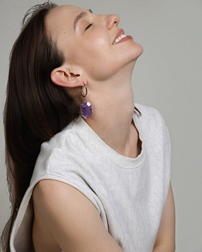 Elsita Jewelry Calm amethyst geometric drop earrings worn by a smiling woman in a white sleeveless top.