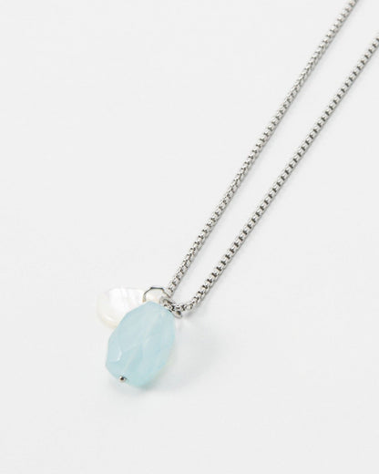 Elsita Jewelry Azul necklace featuring a light blue faceted gemstone and a small white pearl on a silver chain.