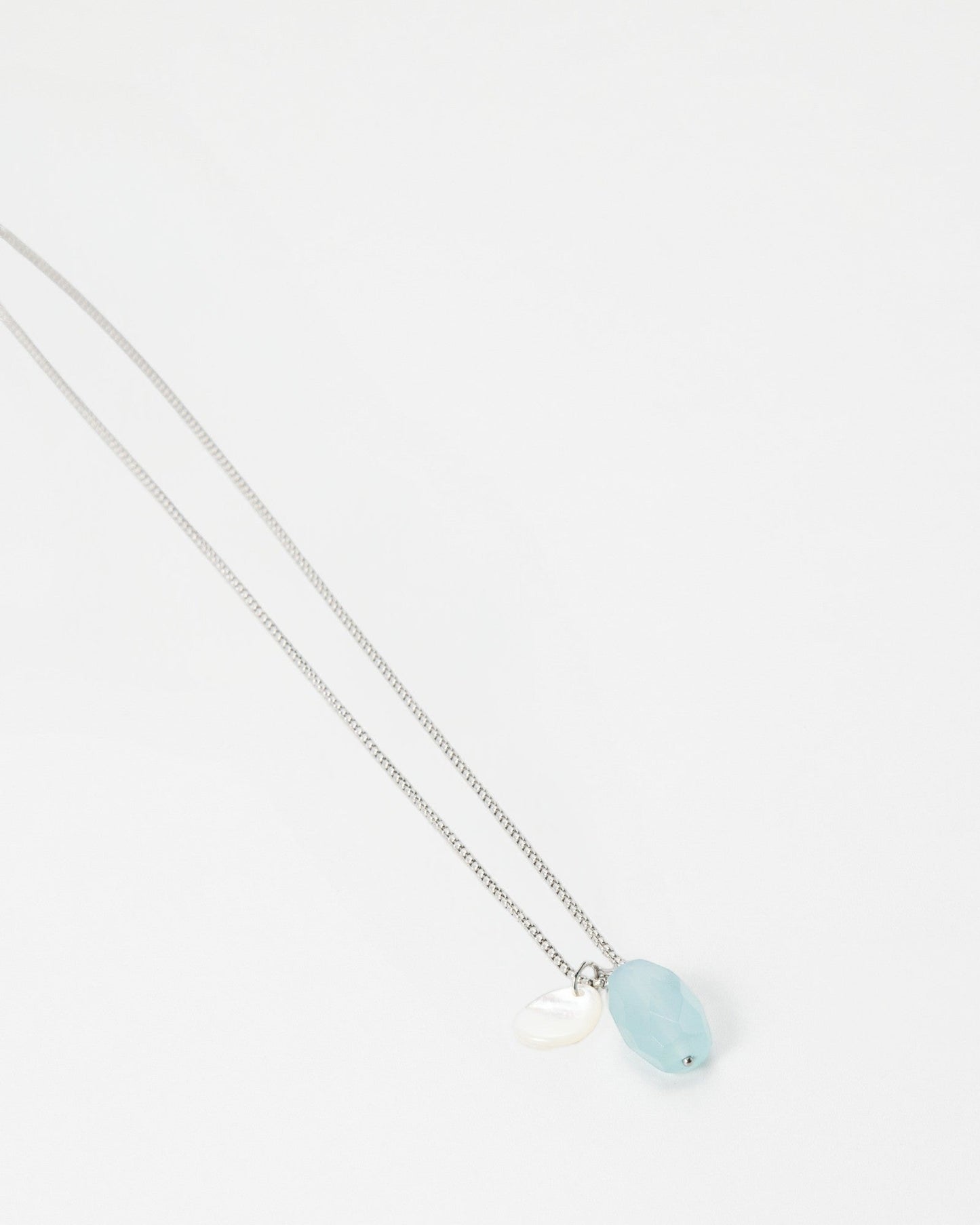 Elsita Jewelry Azul necklace featuring a light blue oval gemstone and a small white shell charm on a silver chain.