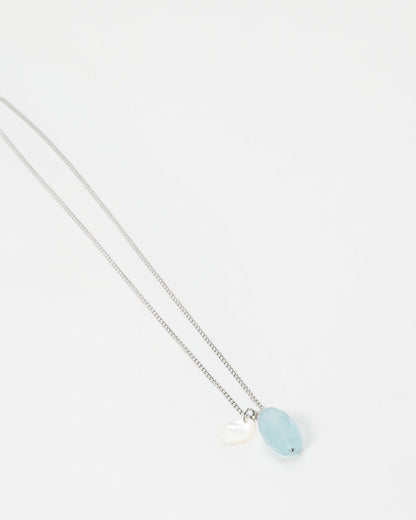 Elsita Jewelry Azul necklace featuring a light blue oval gemstone and a small white shell charm on a silver chain.