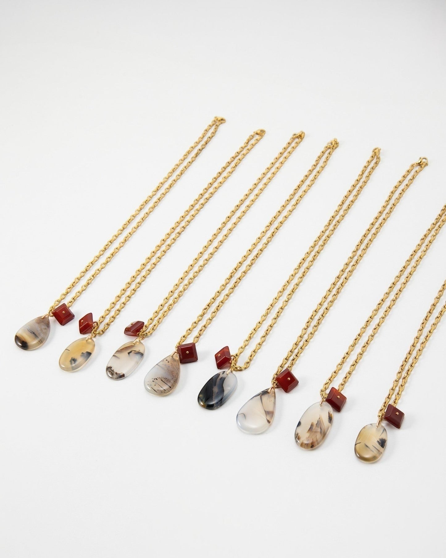Elsita Jewelry Calligraphy necklaces featuring teardrop-shaped agate pendants and small red square beads on gold chains