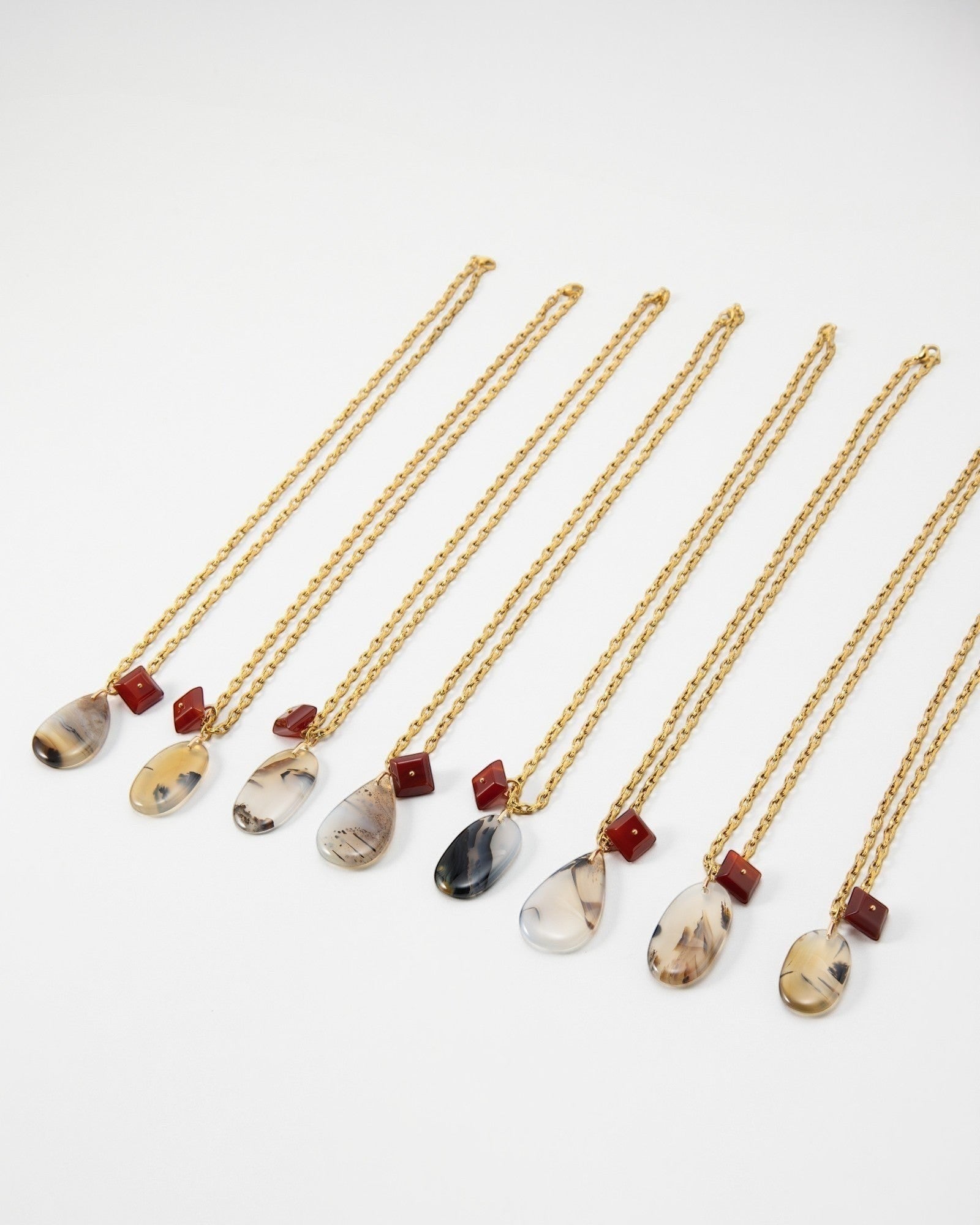 Elsita Jewelry Calligraphy necklaces featuring teardrop-shaped agate pendants and small red square beads on gold chains