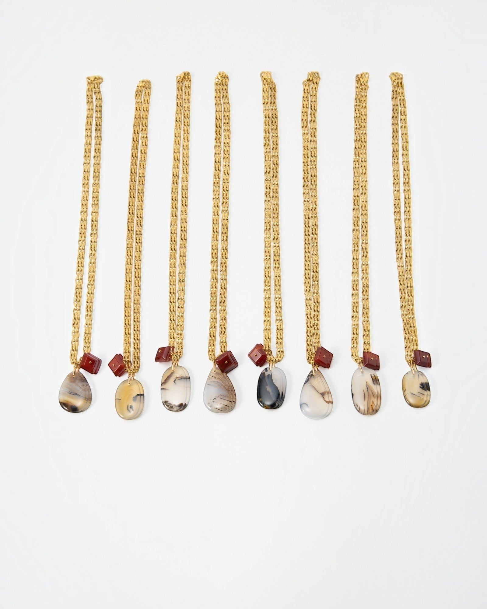 Elsita Jewelry Calligraphy necklaces featuring teardrop-shaped agate pendants and small red beads on gold chains.