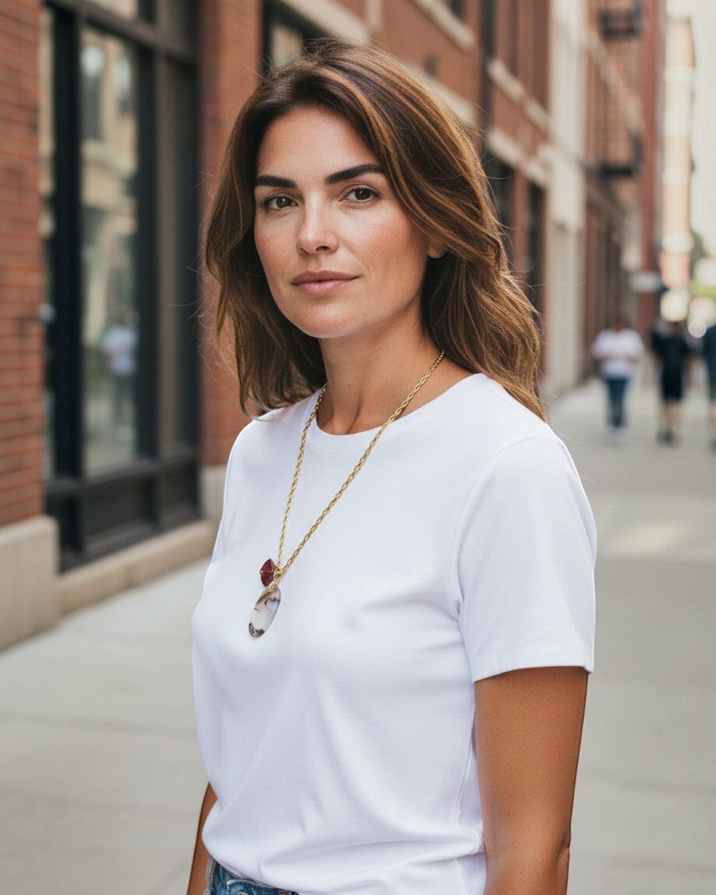 Woman wearing an Elsita Jewelry Calligraphy pendant necklace with a white t-shirt on a city street