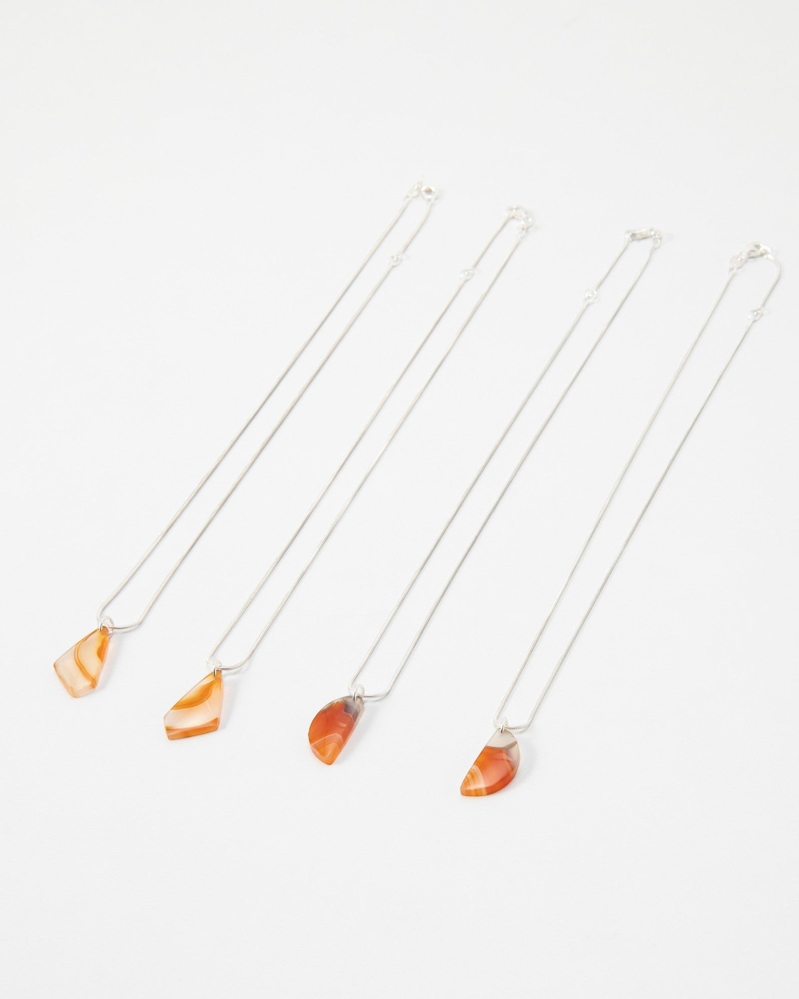 Four Elsita Jewelry Citrus II necklaces featuring polished orange agate pendants on delicate silver chains.