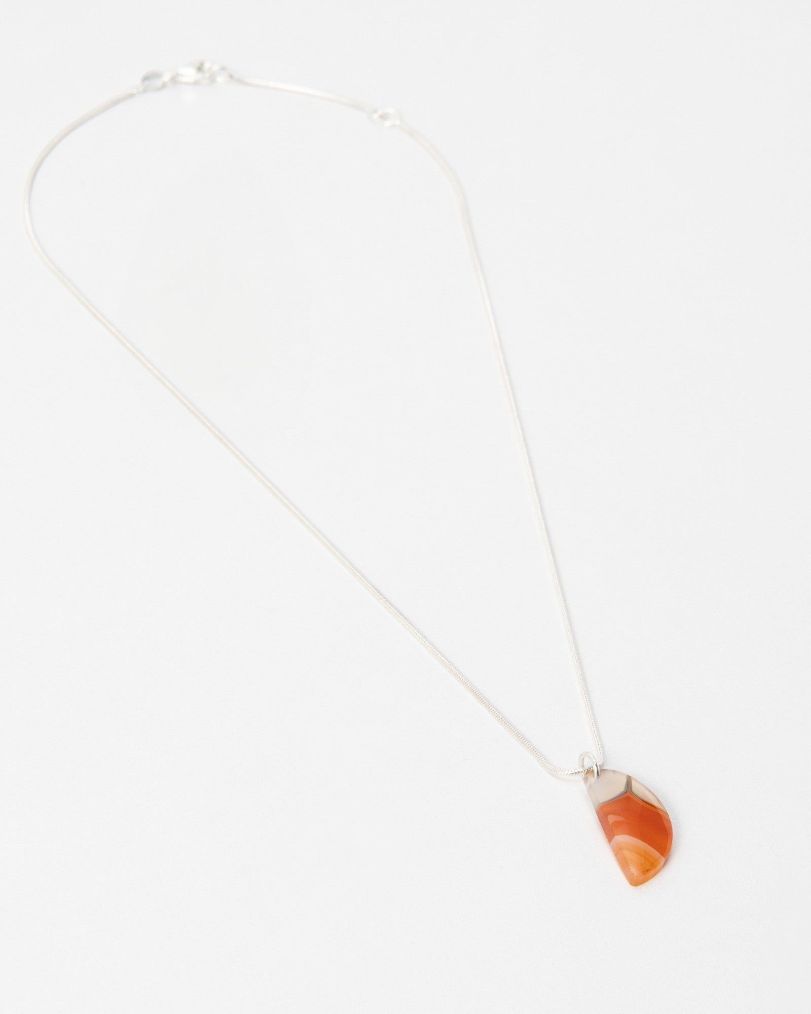 Elsita Jewelry Citrus I necklace featuring a small, semi-circular orange carnelian stone pendant on a silver chain.
