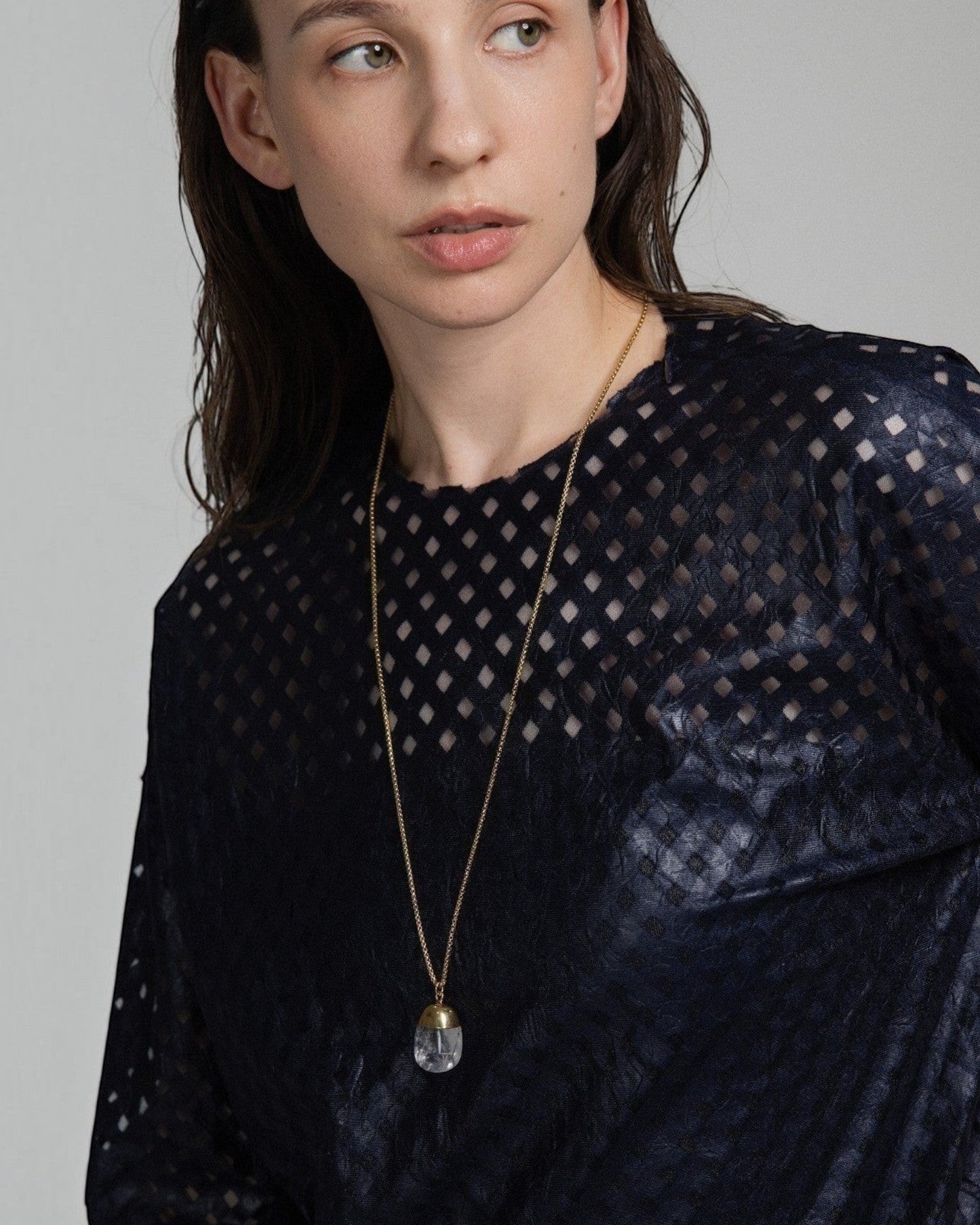 Model wearing an Elsita Jewelry Lustre IV clear quartz pendant necklace with a gold-tone chain on a dark textured top.