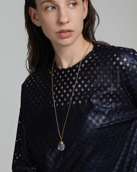 Model wearing an Elsita Jewelry Lustre IV clear quartz pendant necklace with a gold-tone chain on a dark textured top.