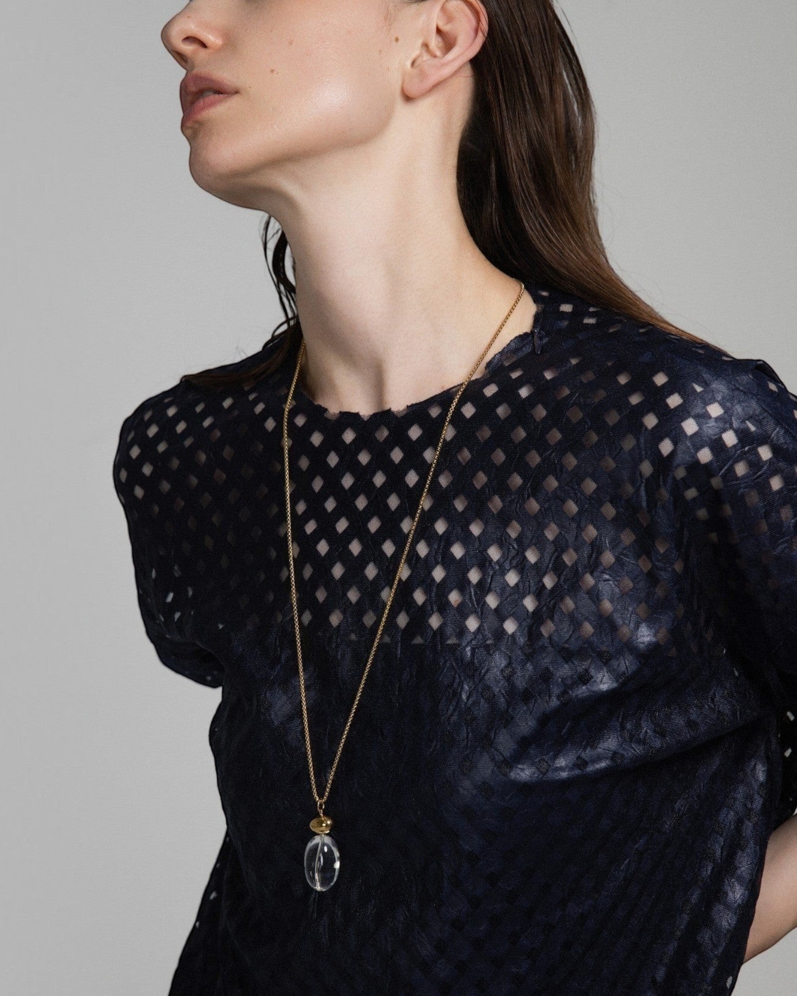 Model wearing an Elsita Jewelry Lustre I necklace featuring a clear quartz pendant on a gold-tone stainless steel chain.