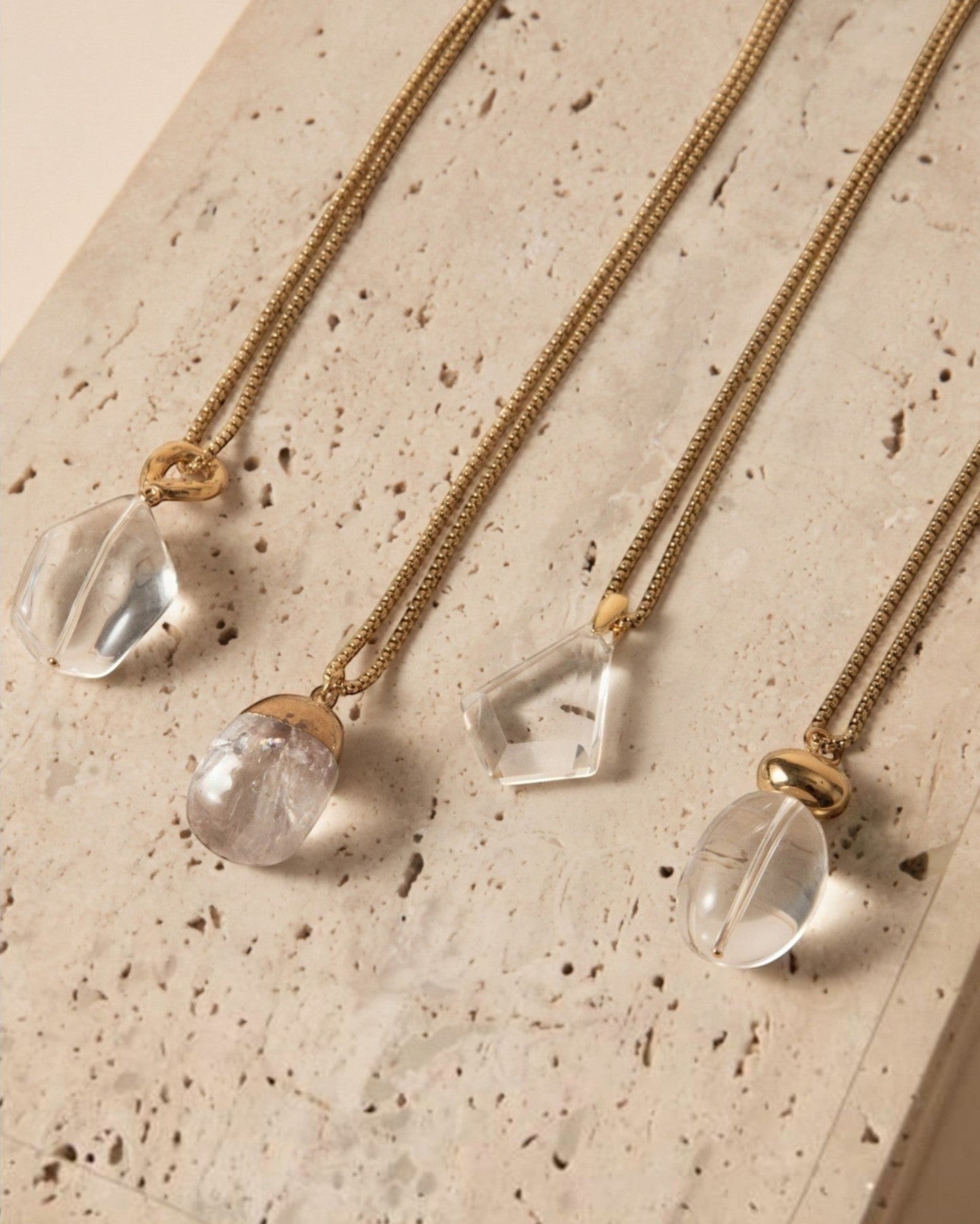 Elsita Jewelry Lustre IV collection featuring four unique clear quartz pendants on gold-toned stainless steel chains.