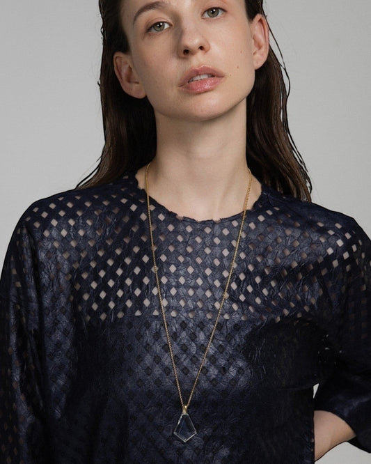 Model wearing an Elsita Jewelry Lustre III clear quartz pendant necklace with a gold chain on a dark textured top.