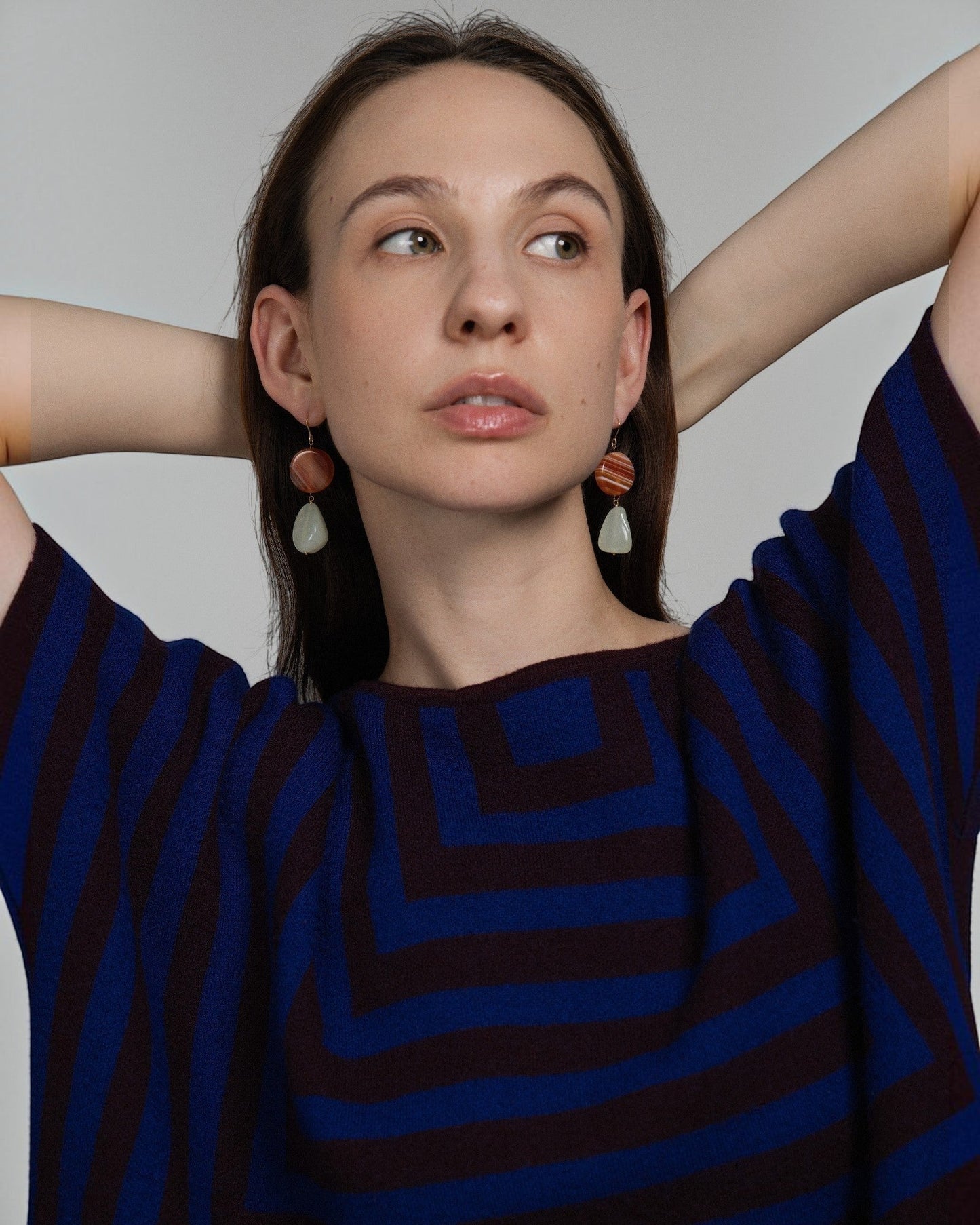 Model wearing Elsita Jewelry Dawn earrings featuring round red banded agate and triangular green Xiuyan jade on gold.
