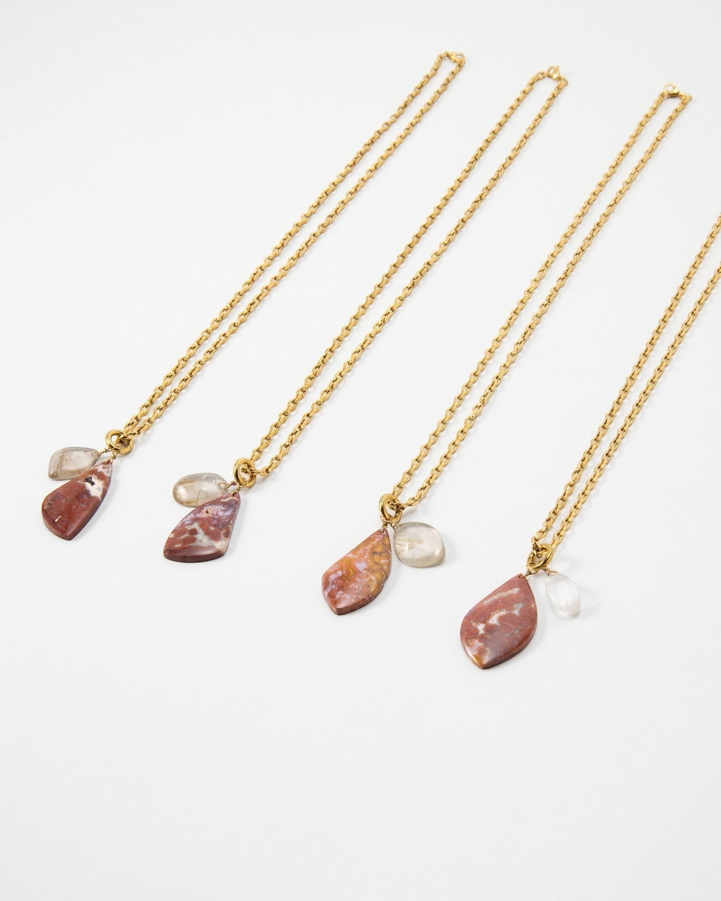 Elsita Jewelry Drift necklaces featuring gold chains with dangling red jasper and clear quartz stone pendants.