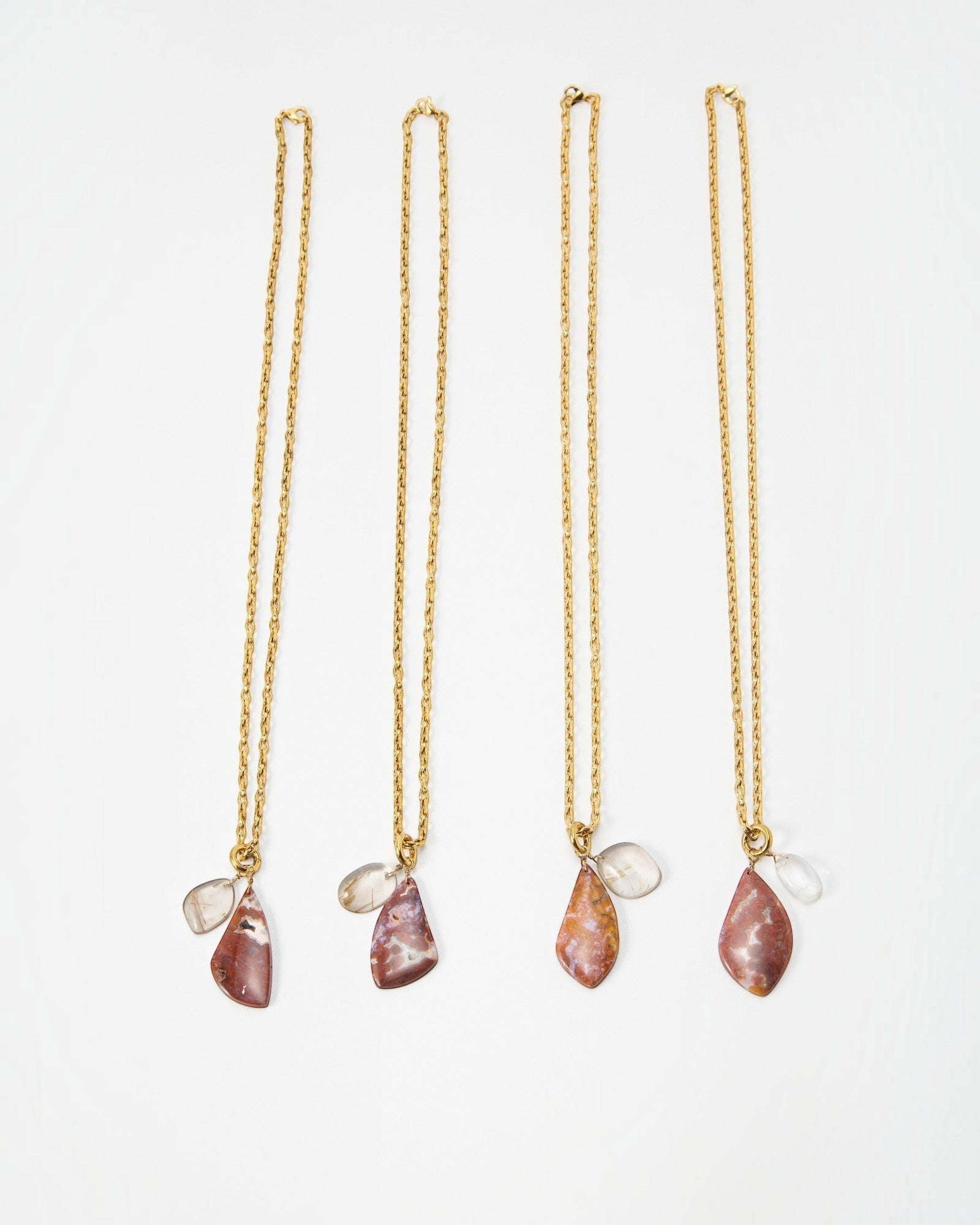 Four Elsita Jewelry Drift necklaces featuring gold chains and multi-colored stone pendants on a white background.