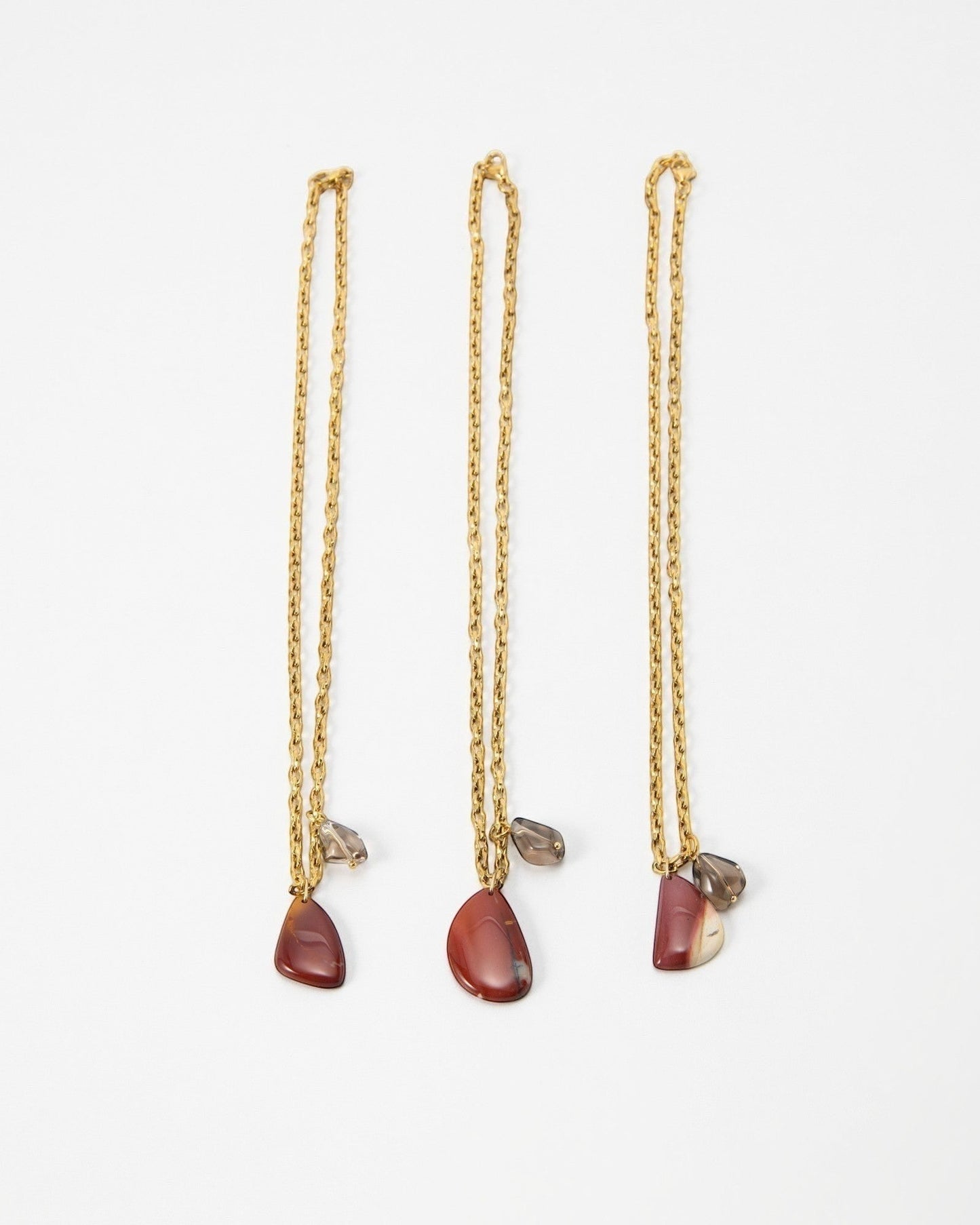 Three Elsita Jewelry Ember gold chain necklaces featuring teardrop-shaped red jasper and small smoky quartz charms.