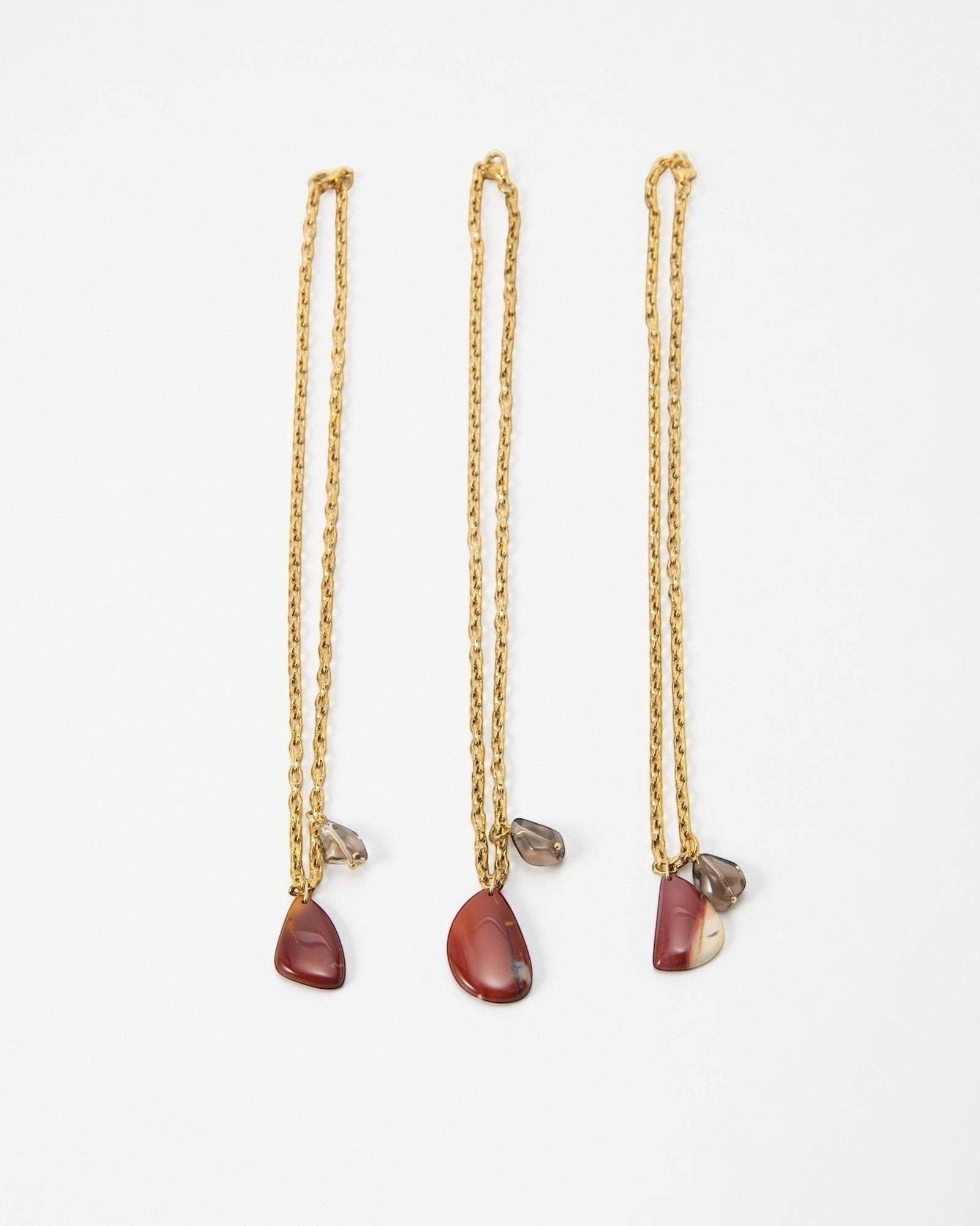 Three Elsita Jewelry Ember gold chain necklaces featuring teardrop-shaped red jasper and small smoky quartz charms.