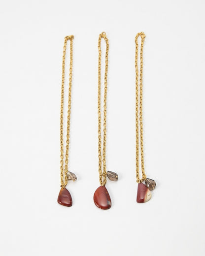 Three Elsita Jewelry Ember gold chain necklaces featuring teardrop-shaped red jasper and small smoky quartz charms.