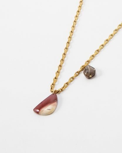 Elsita Jewelry Ember necklace featuring a gold chain with a crescent-shaped red stone and a small grey accent charm.