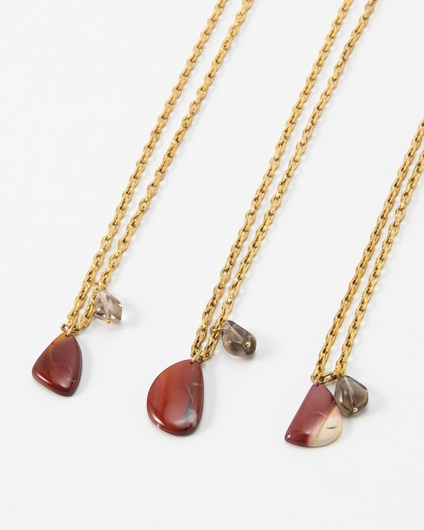 Elsita Jewelry Ember necklaces featuring gold chains with red teardrop stone pendants and small grey crystal accents.