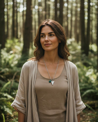 Woman wearing an Elsita Jewelry Forest triangle pendant necklace with a green stone in a sunlit forest setting.