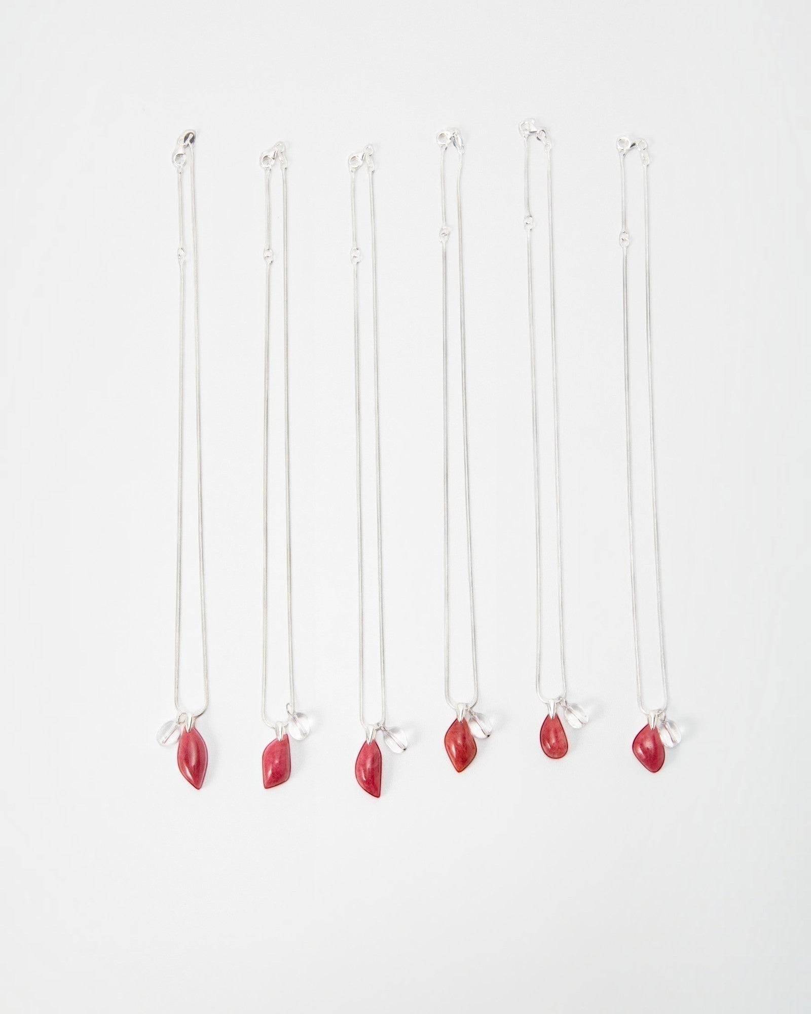 Six Elsita Jewelry Fuchsia necklaces featuring silver chains with small red teardrop pendants and clear crystal charms.