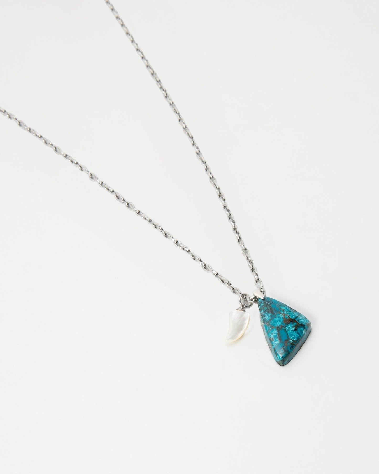Elsita Jewelry Lagoon I necklace featuring a triangular blue stone pendant and a small white horn charm on a chain