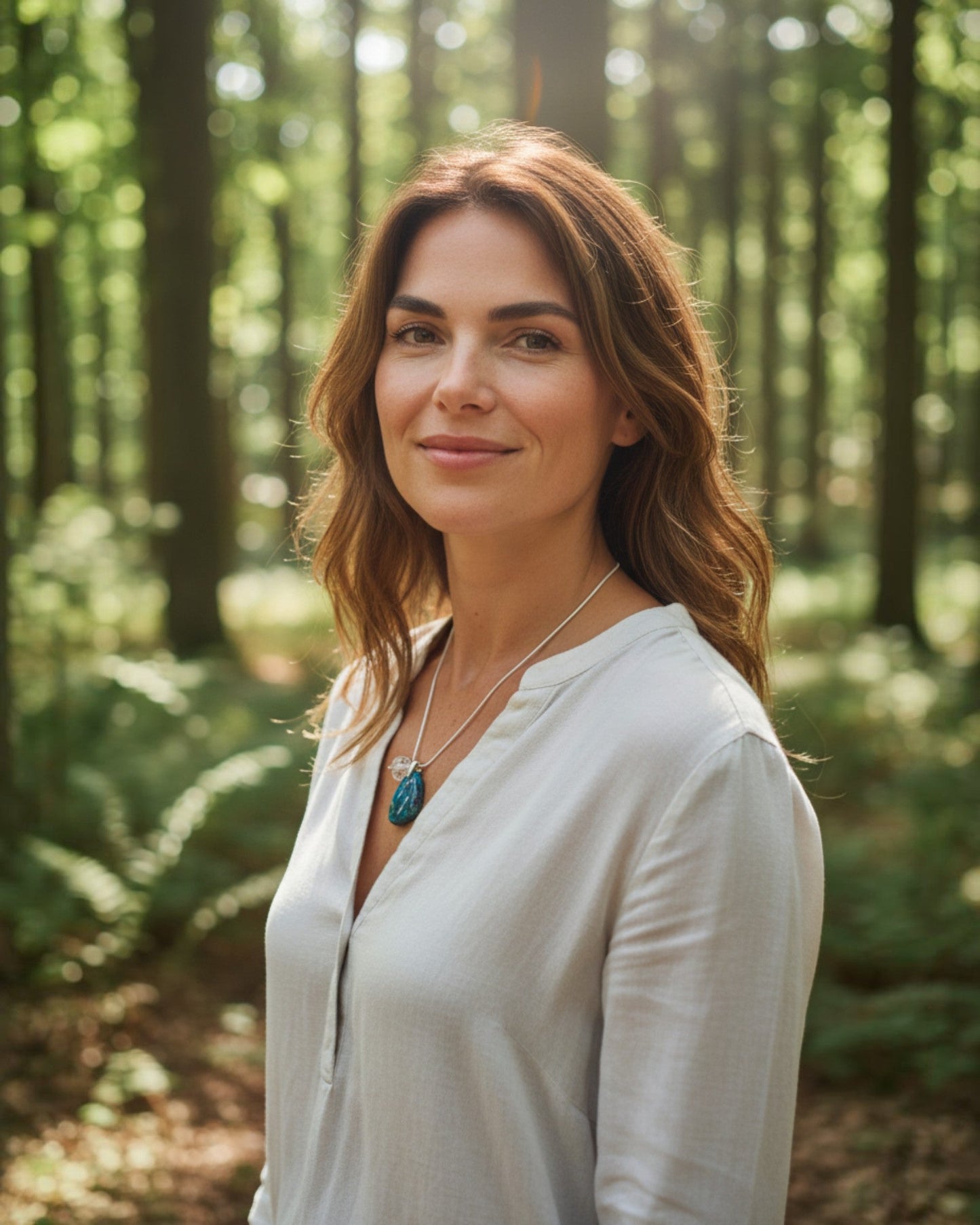 Woman wearing an Elsita Jewelry Marine pendant necklace with a blue stone in a sunlit forest setting.