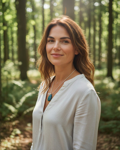 Woman wearing an Elsita Jewelry Marine pendant necklace with a blue stone in a sunlit forest setting.