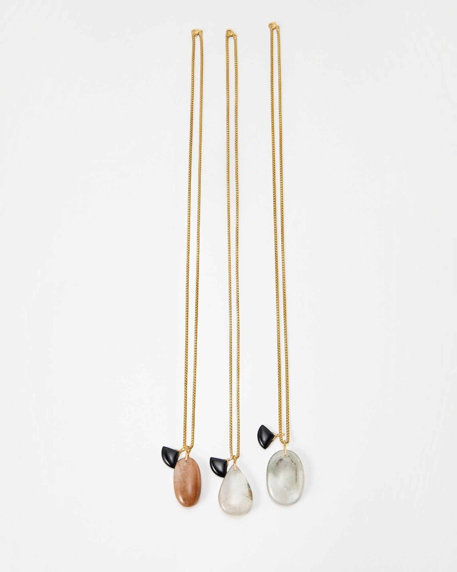 Elsita Jewelry Mist I necklaces featuring gold chains with dangling smooth stone pendants and small black accents