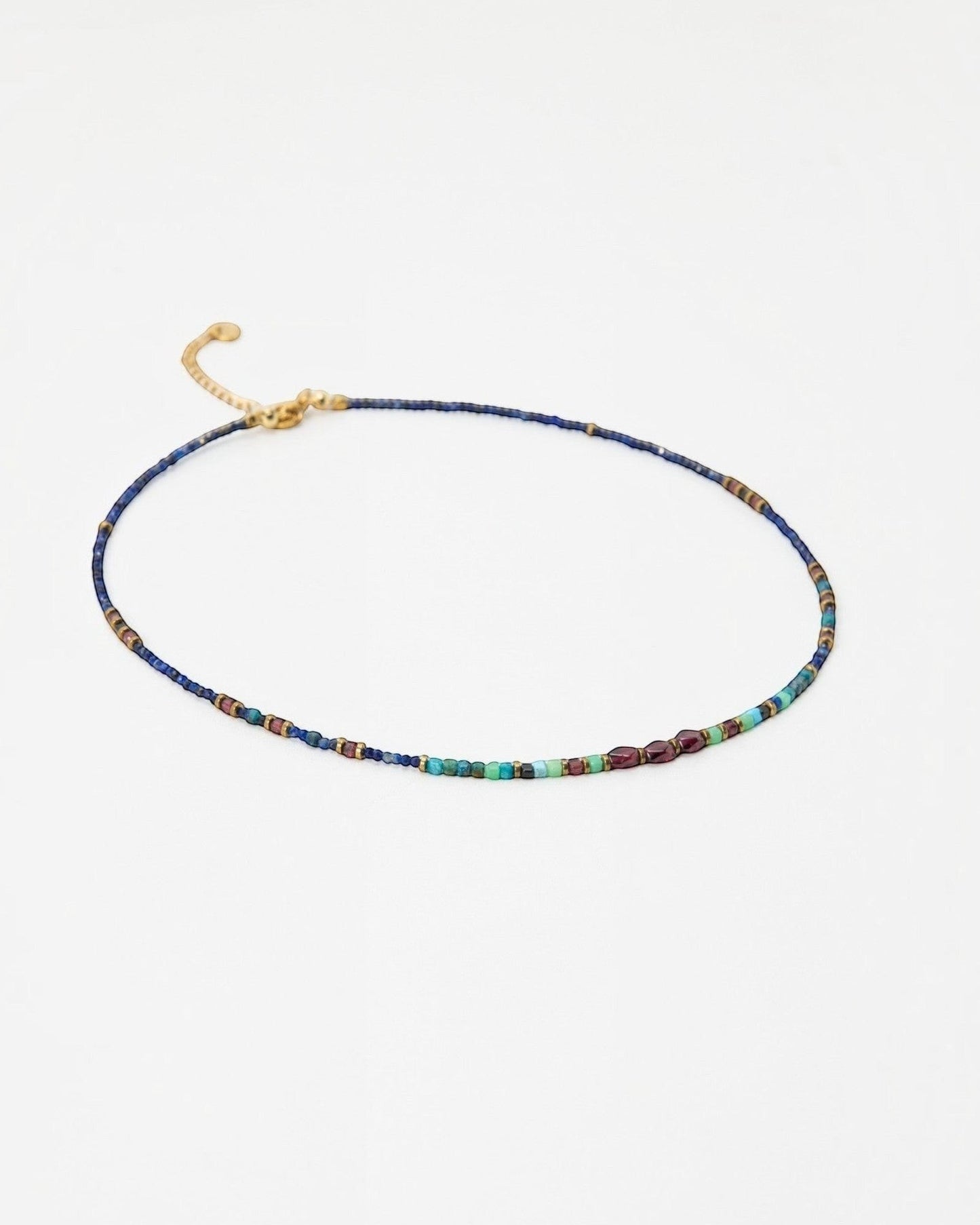 Elsita Jewelry Nomad beaded choker necklace with blue lapis, turquoise, and garnet stones on a gold chain.