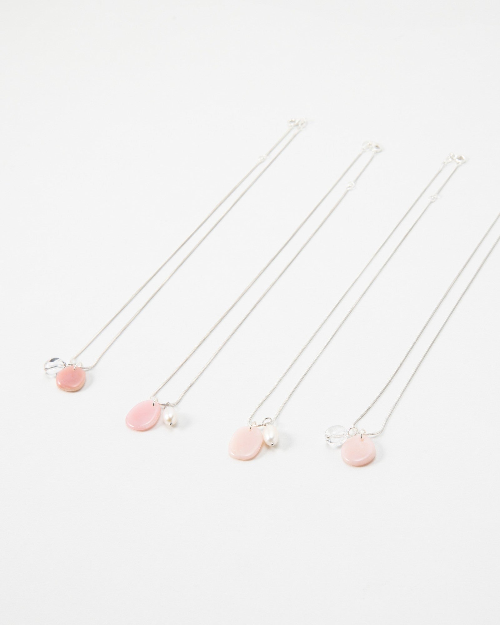 Four Elsita Jewelry Petal Clear necklaces featuring delicate silver chains with pink petal charms and pearl accents.
