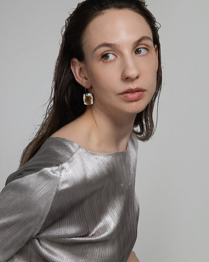 Model wearing Elsita Jewelry Wild 20 raw Indonesian agate earrings on 14K gold-filled hoops against a grey background.