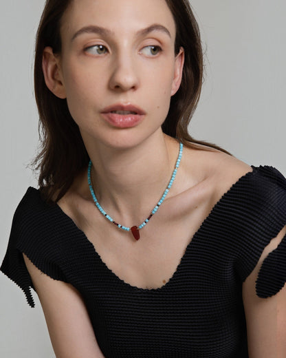 Elsita Jewelry Pixel necklace featuring turquoise cube beads and a red agate pendant worn by a model in a black top.